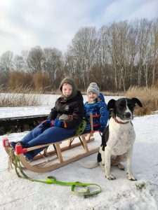 LucaKutya és két gyerek, akik szánkón ülnek, egy befagyott tó előtt ülnek télen a hóban