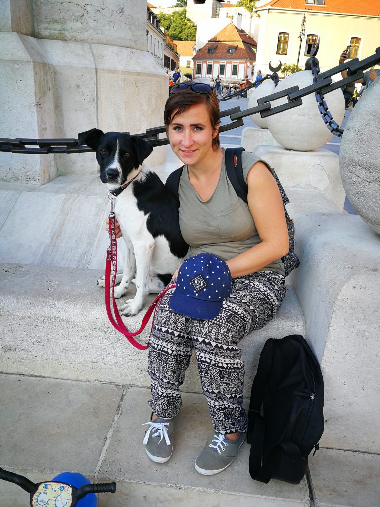 LucaKutya egy városban kirándul. Egy szobor előtt ülnek a gazdájával.